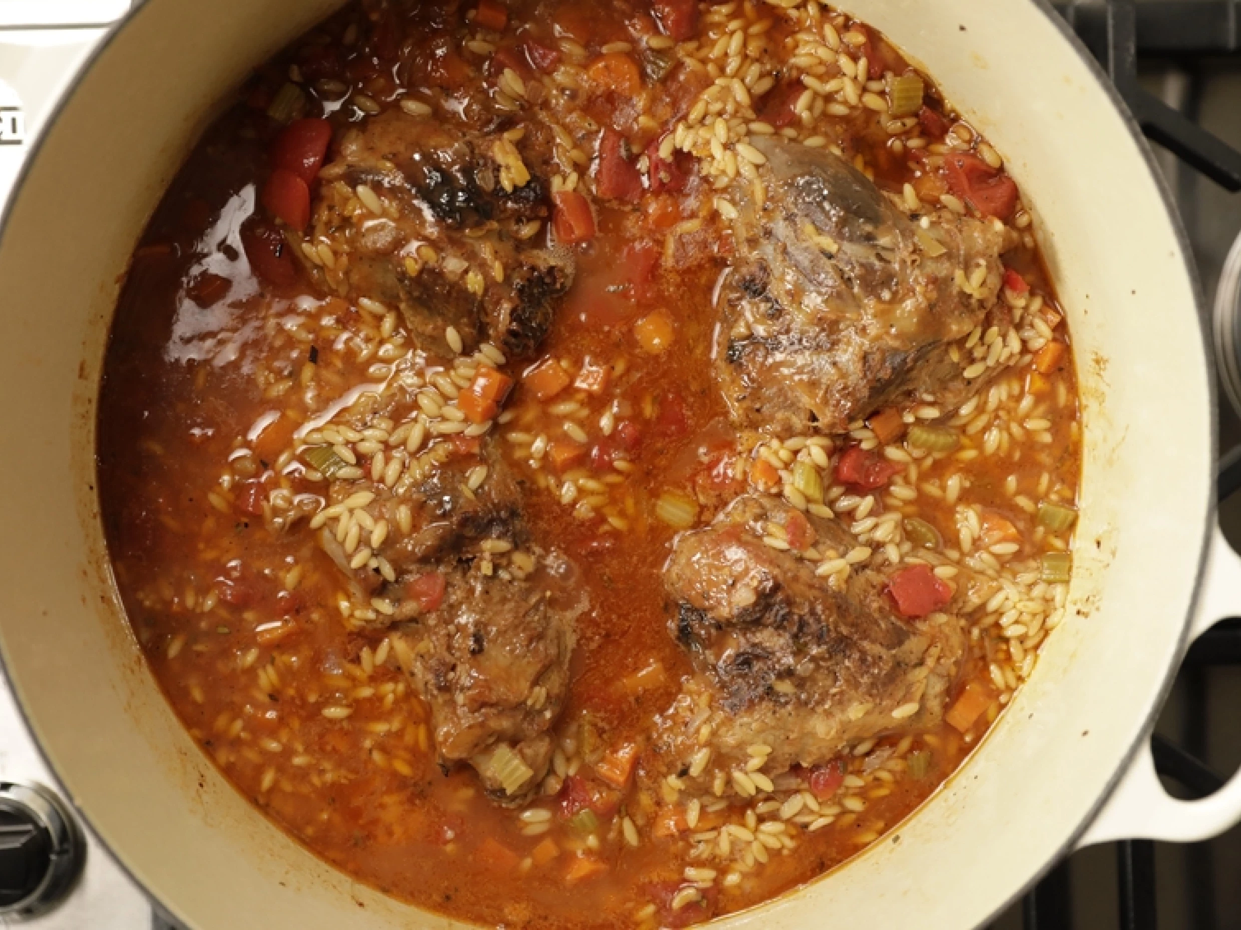 lamb shanks in a dish with tomato and orzo