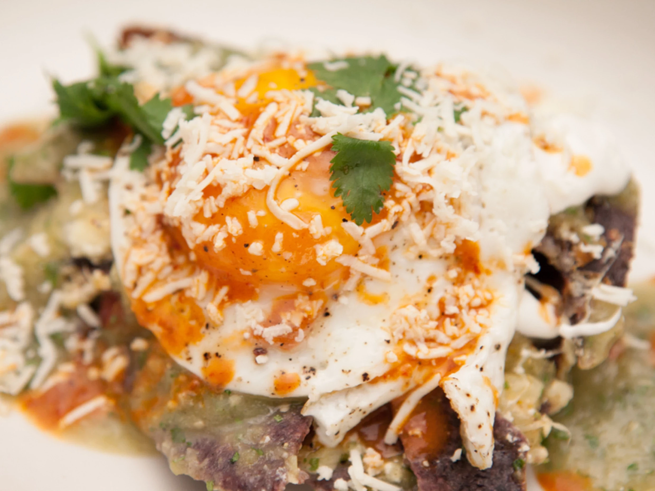 a dish of chilaquilos drizzled in a tomatillo sauce and topped with an egg.