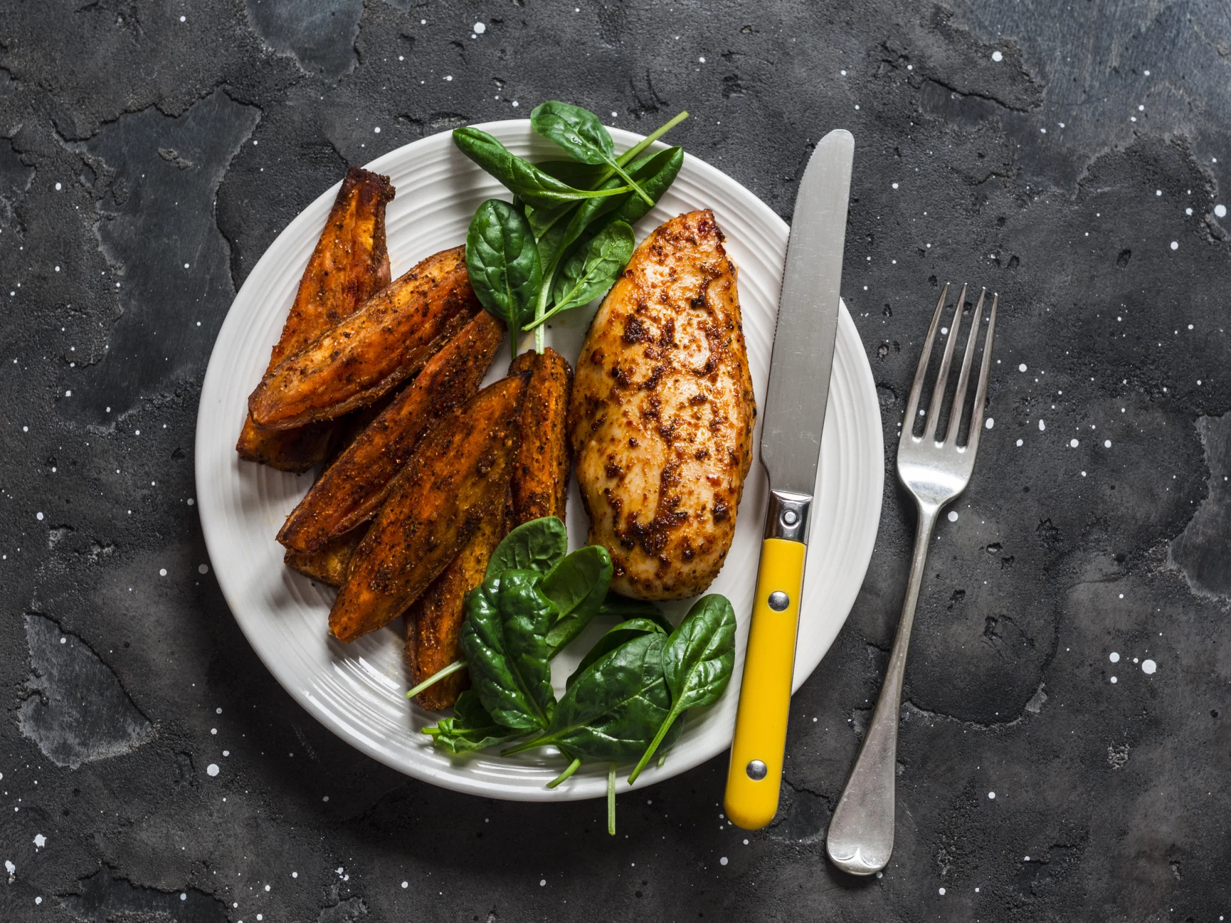 A plate of buffalo-coated chicken with roasted sweet potatoes