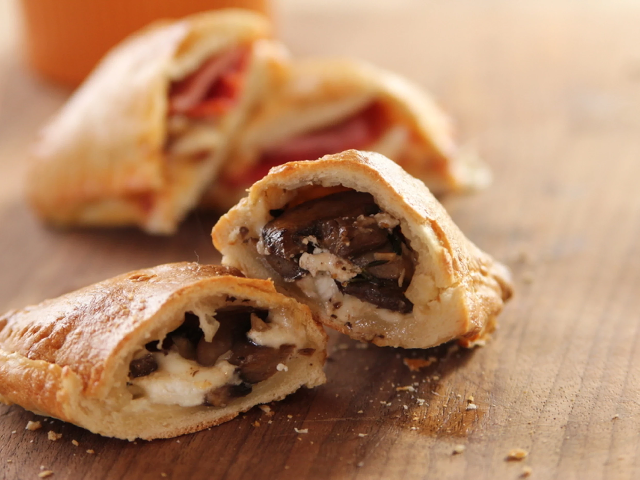 an image of pizza pockets on a wooden table stuffed with cheese and sautéd mushrooms