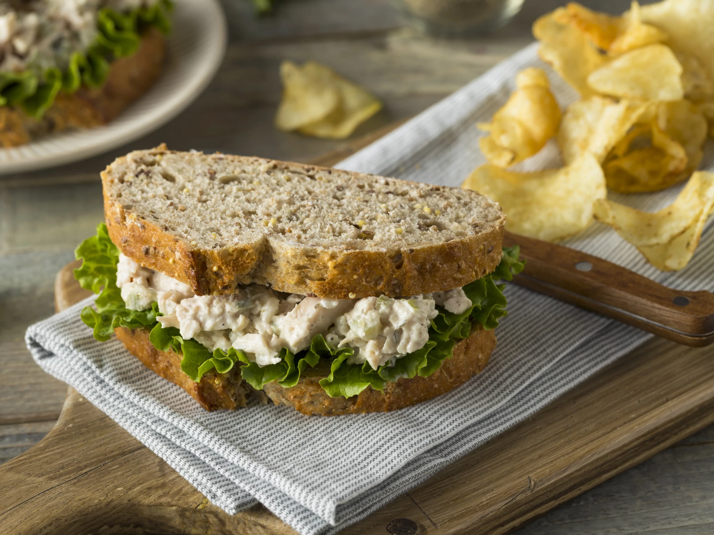 chicken salad sandwich with extra mayonaisse sitting on a chopping board beside some crisps