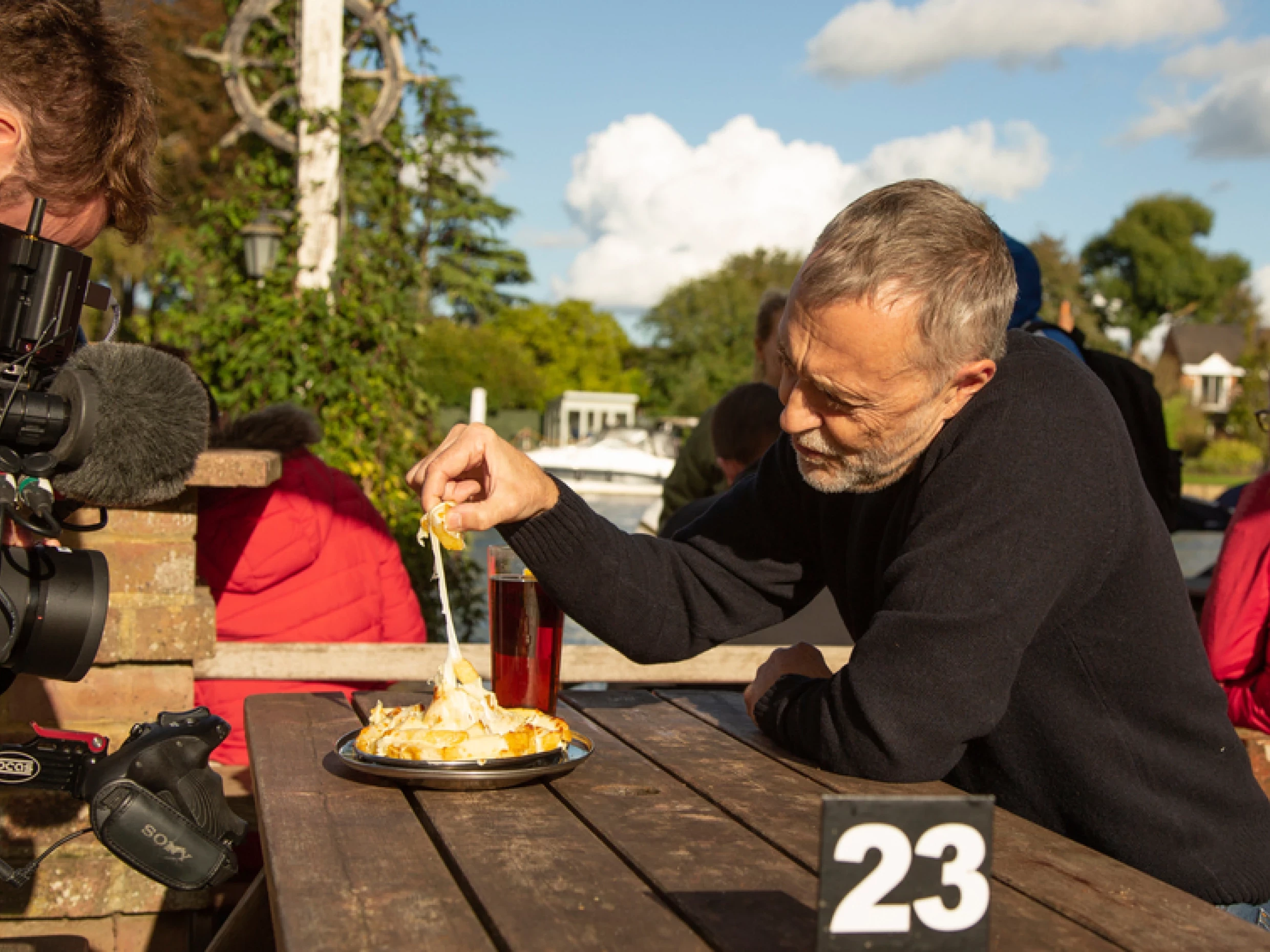 Michel Roux Jnr outside The Bounty riverside at picnic table, with camera crew in shot